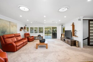 A spacious living room with a leather sofa, a coffee table, and a TV on a wooden stand.