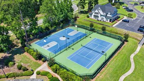 Vista aérea de un complejo de canchas de tenis con dos canchas, rodeado de césped cuidado y árboles.