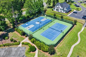 Vue aérienne d’un complexe de courts de tennis comprenant deux terrains, entourés de pelouses et d’arbres bien entretenus.
