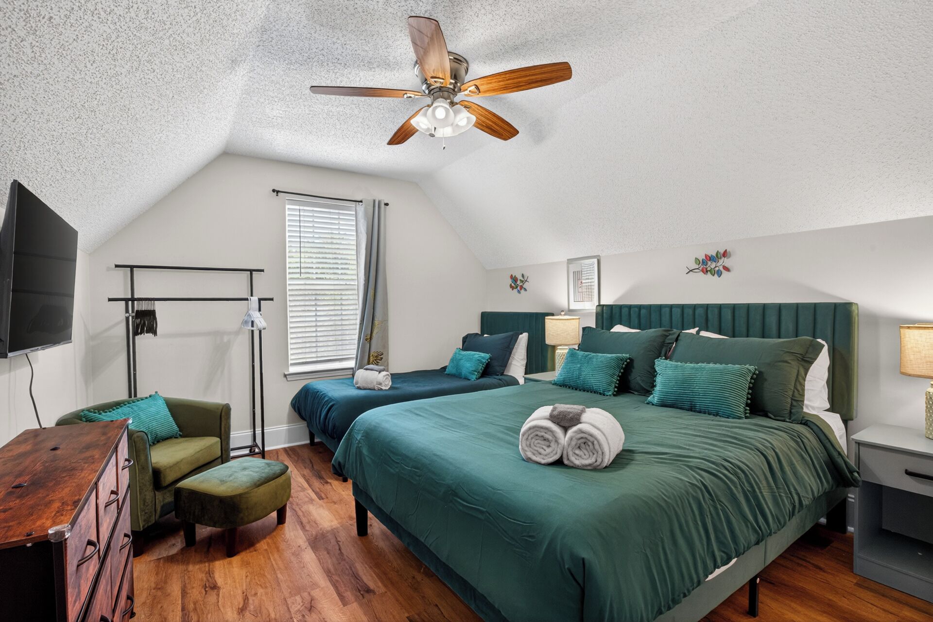 A bedroom with two beds, a ceiling fan, a TV, a desk, and a chair.