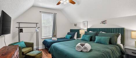 A bedroom with two beds, a ceiling fan, a TV, a desk, and a chair.