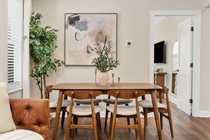 Un comedor con una mesa de madera, seis sillas, una planta en maceta, un cuadro y un televisor al fondo.