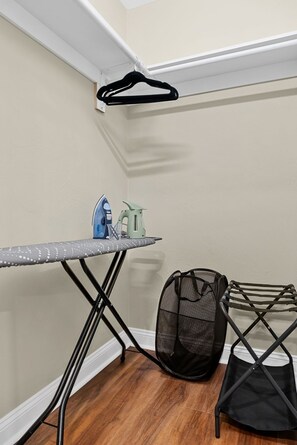 A corner of a room with a wooden floor, a small ironing board with an iron and a spray bottle, a black mesh bag, and a black hanger on a white ceiling. - Fabulous 6-bedroom apartment with AC in vibrant Somerville (Somerville)