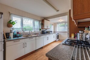 Eine moderne Küche mit weißen Schränken, einer Granit-Arbeitsplatte, einem eingebauten Backofen und einem Fenster mit Jalousien.