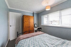 Ein Schlafzimmer mit einem Bett, einem Holzschrank, einem Schreibtisch mit Stuhl, einem Fenster mit Jalousien und einer Deckenleuchte.