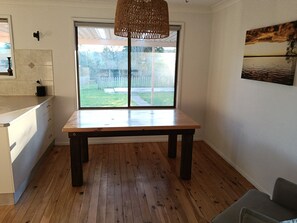 A room with a wooden table, a hanging light fixture, a window with a view of the outdoors, and a painting on the wall.