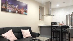 A modern living room with a black sofa, a glass coffee table, and a cityscape painting on the wall. - NEW 2B Duplex near Sport Complex & Airport Unit-A (Philadelphia)