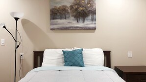A bedroom with a bed, a nightstand, a painting on the wall, and a floor lamp. - NEW 2B Duplex near Sport Complex & Airport Unit-A (Philadelphia)