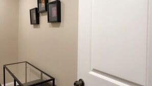 A hallway with a glass table, a white door, and three framed pictures on the wall. - NEW 2B Duplex near Sport Complex & Airport Unit-A (Philadelphia)
