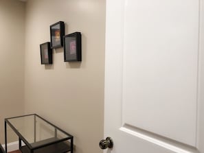 Un pasillo con una mesa de vidrio, una puerta blanca y tres cuadros en la pared.