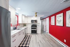 Une cuisine avec des meubles blancs, un réfrigérateur noir, un mur rouge et des illustrations de poissons encadrées.