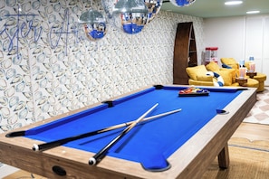 Une table de billard avec des queues de billard, un tapis bleu et un papier peint à motifs représentant des poissons.