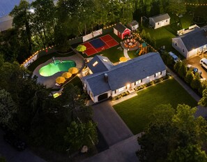 An aerial view of a residential property with a swimming pool, a tennis court, a patio with umbrellas, and a house with a garage. - Pool+HotTub+Pickleball+Game+Movie+PlayRoom+PetsOK (Barnstable)