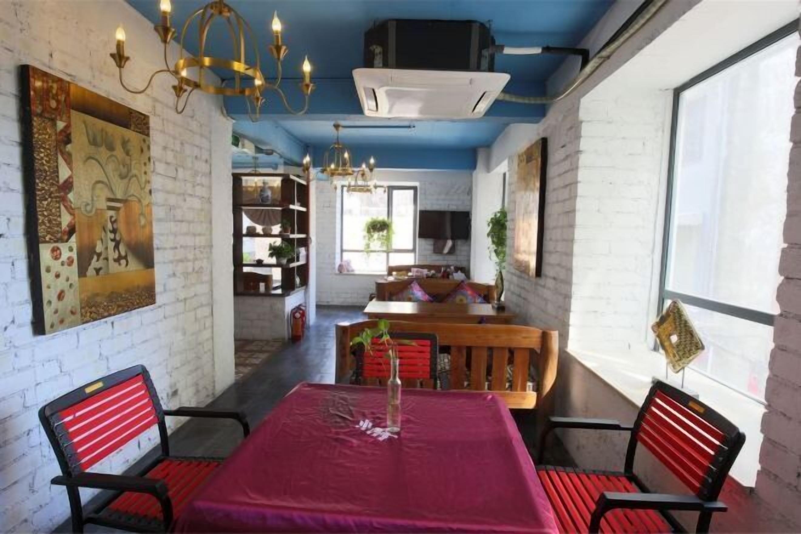 A dining area with a red tablecloth, black and red chairs, a chandelier, and a white brick wall.