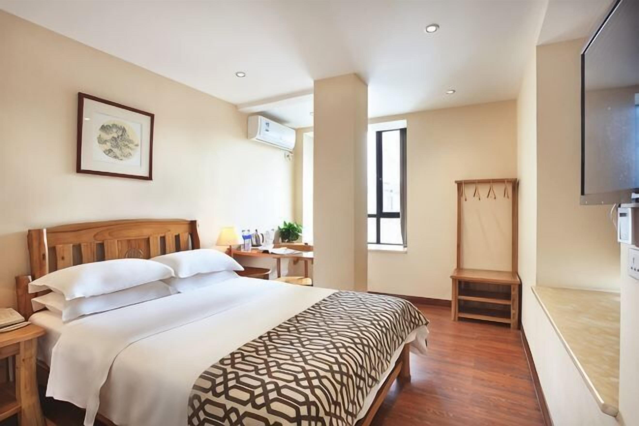 A hotel room with a bed, bedside table, TV, and a window.