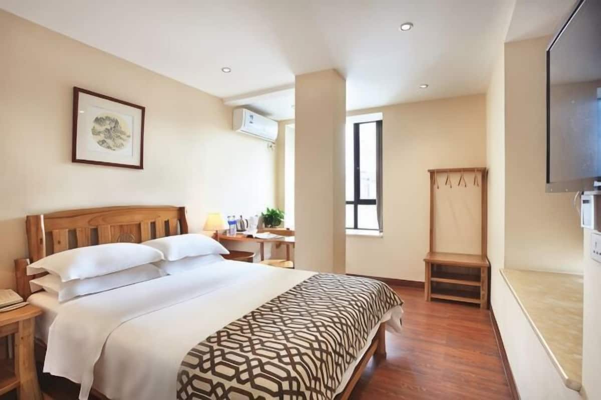 A hotel room with a bed, bedside table, TV, and a window.