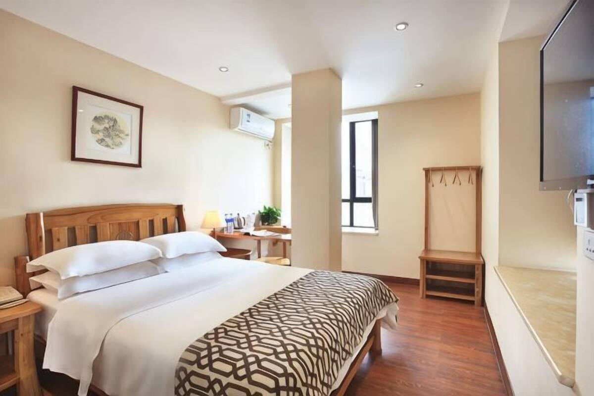 A hotel room with a bed, bedside table, TV, and a window.