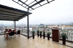 A balcony with a view of a cityscape, a table with chairs, and potted plants. - Jinfeng Hotel (Guilin)