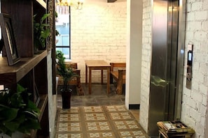 A narrow hallway with a brick wall, a wooden table and chairs, a potted plant, and an elevator.