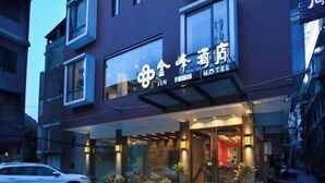 A hotel entrance with a glass facade, potted plants, and a car parked outside. - Jinfeng Hotel (Guilin)