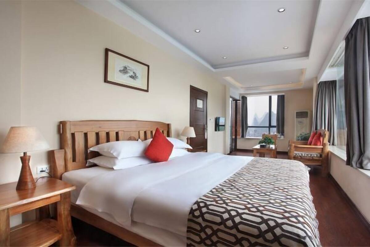 A hotel room with a large bed, bedside tables, a window, and a view.