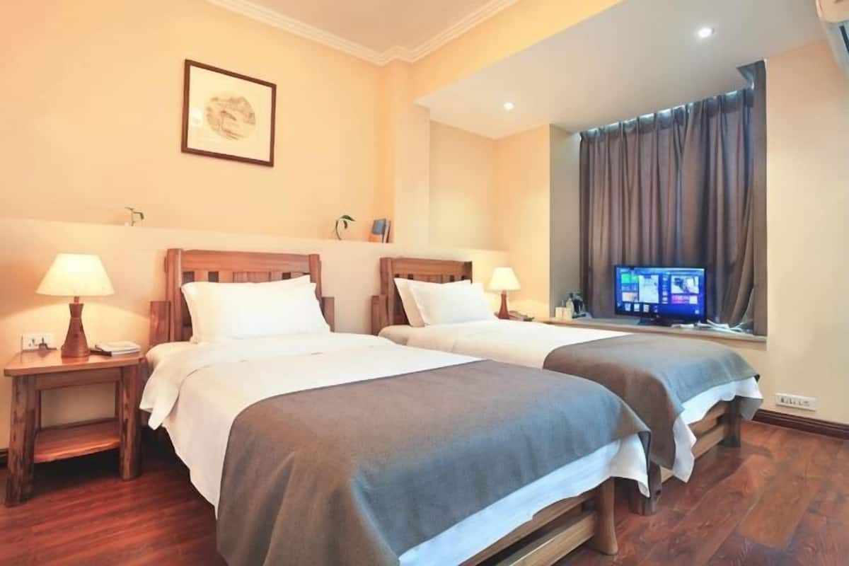 A hotel room with two beds, bedside lamps, a television, and a window with curtains.