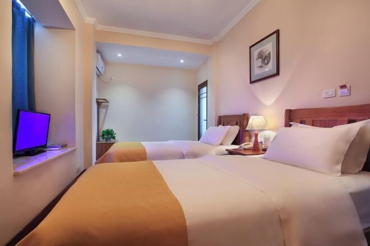 A hotel room with two beds, a desk with a laptop, a lamp, and a framed picture on the wall.