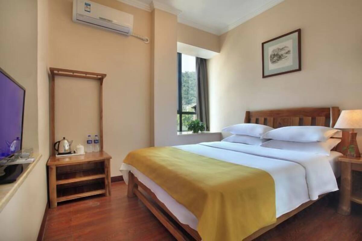 A hotel room with a bed, bedside table, TV, and window.