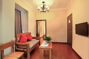 A room with a bed, a table with a plant, a mirror, a TV, and a door.