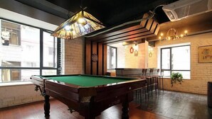 A pool table in a room with wooden flooring, large windows, and a brick wall. - Jinfeng Hotel (Guilin)