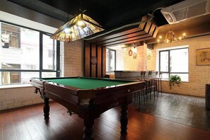 A pool table in a room with wooden flooring, large windows, and a brick wall. - Jinfeng Hotel (Guilin)