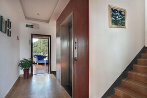 A hallway with a wooden floor, a blue chair, a potted plant, and a staircase. - Jinfeng Hotel (Guilin)
