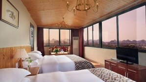 A hotel room with two beds, a TV, a wooden ceiling, and a large window with a city view. - Jinfeng Hotel (Guilin)