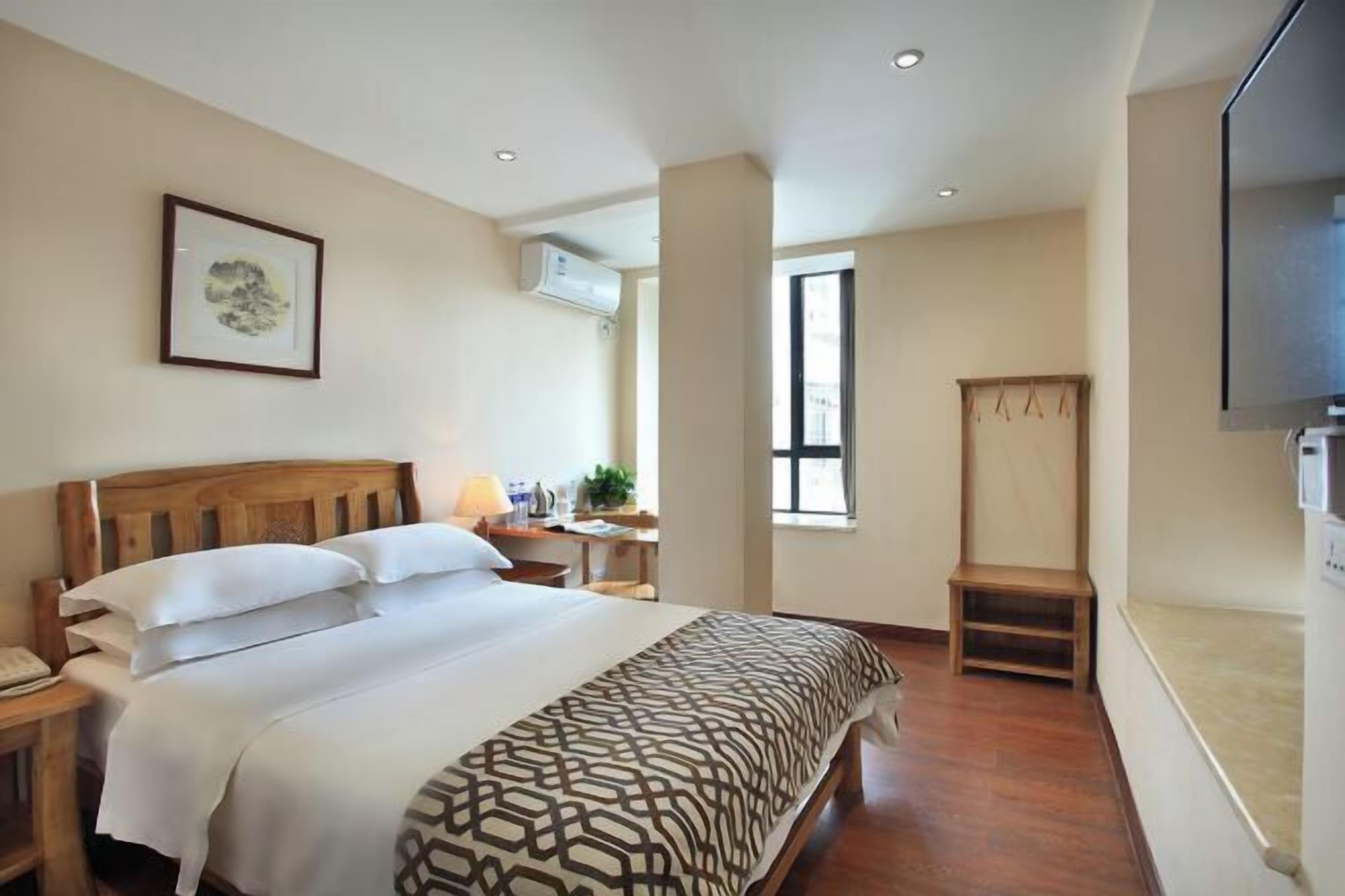 A hotel room with a bed, bedside table, lamp, TV, and a window.