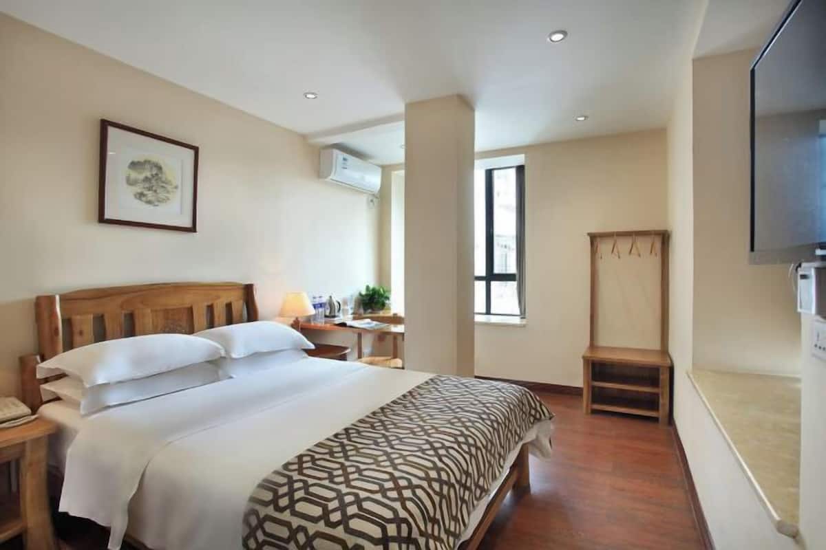 A hotel room with a bed, bedside table, lamp, TV, and a window.