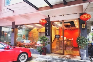 A hotel entrance with a red car parked outside, potted plants, and a red lantern. - Jinfeng Hotel (Guilin)