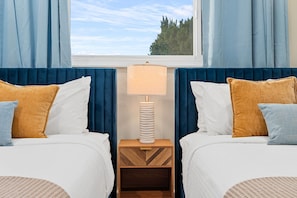 Ein Hotelzimmer mit zwei Betten, einem Nachttisch mit Lampe und einem Fenster mit Vorhängen.
