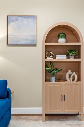 Ein Zimmer mit einem Holzbogenschränkchen, einem gerahmten Landschaftsbild und einem blauen Sessel.