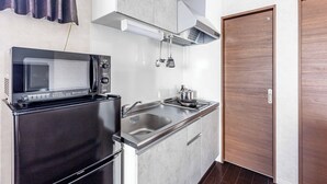 A compact kitchen with a microwave, stove, sink, and wooden door. - FDS Panache (OSAKA/NISHINARIKU/HANAZONOMINAMI)