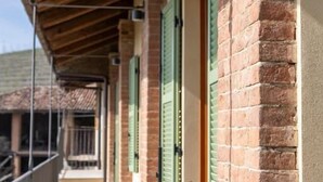 A covered balcony with brick walls and green shutters, potted plants, and a railing. - Be Langhe in Monforte (Monforte d'Alba)
