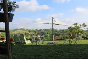An outdoor seating area with a table and chairs, a white umbrella, and a view of rolling hills in the background. - Be Langhe in Monforte (Monforte d'Alba)
