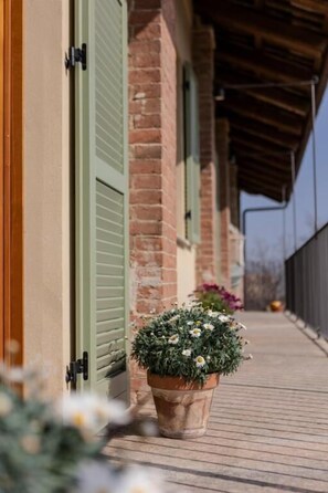 A brick building with green shutters, a wooden deck, and a potted plant with white flowers. - Be Langhe in Monforte (Monforte d'Alba)