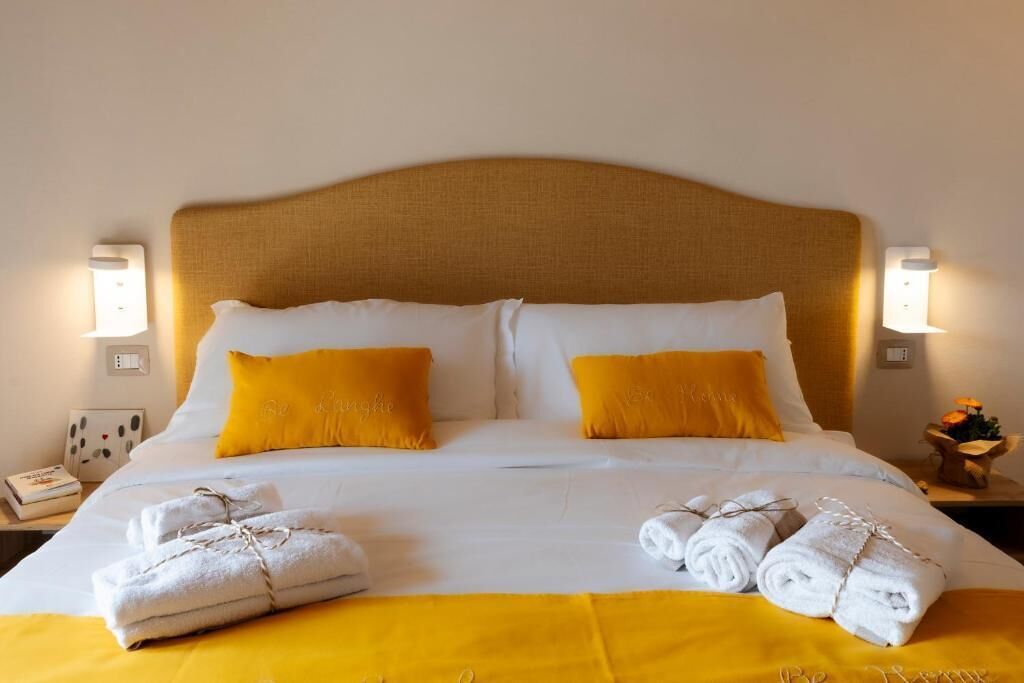 A hotel room with a large bed, two pillows, a bedside table with a lamp, and towels on the bed.