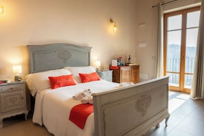 Un lit bien fait, avec une literie blanche et rouge, une table de chevet avec une lampe, et une vue sur lâextĂ©rieur par une porte vitrĂ©e.