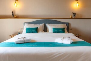 Una cama bien hecha con dos almohadas, un edredón color aguamarina y una toalla al lado.