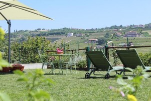 Un patio con una mesa y sillas, un carretón, y vistas a colinas onduladas y edificios.