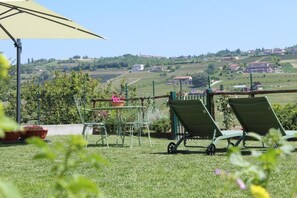A patio with a table and chairs, a wheelbarrow, and a view of rolling hills and buildings. - Be Langhe in Monforte (Monforte d'Alba)