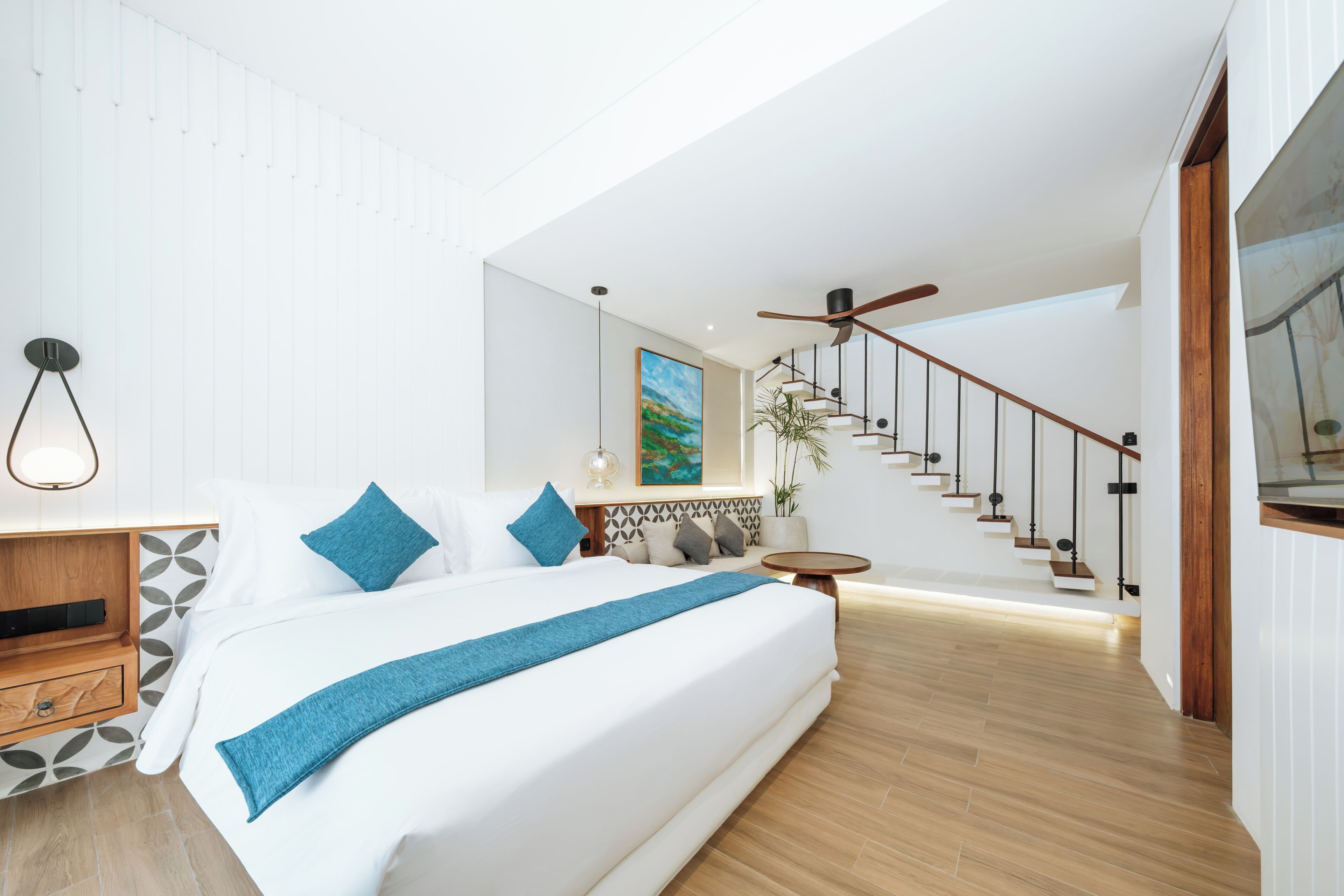 Un dormitorio moderno con una cama grande, una mesita de noche de madera, una mesa redonda y una escalera que sube a un nivel superior.
