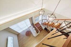 A spacious interior with a wooden staircase, a round wooden table, and a sofa. - Nuho Living (Pecatu)