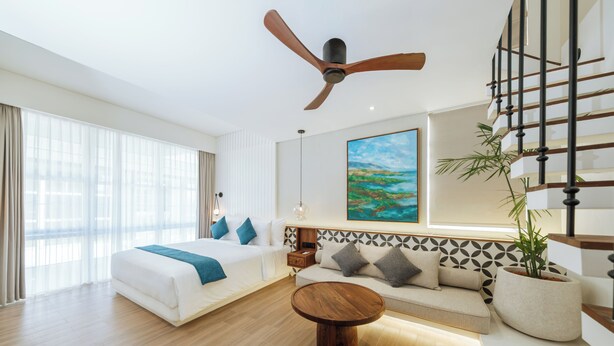 A hotel room with a bed, sofa, coffee table, and a painting on the wall. - Nuho Living (Pecatu)